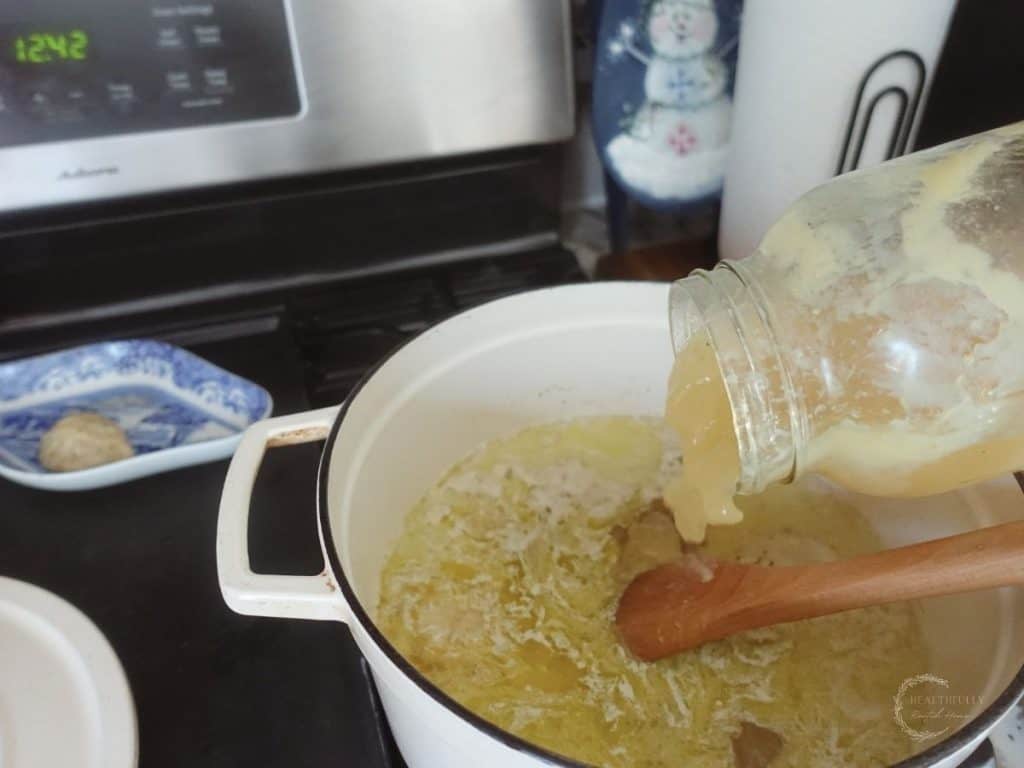 pouring bone broth into a white dutch oven with blue and white china plate on the stove next to it