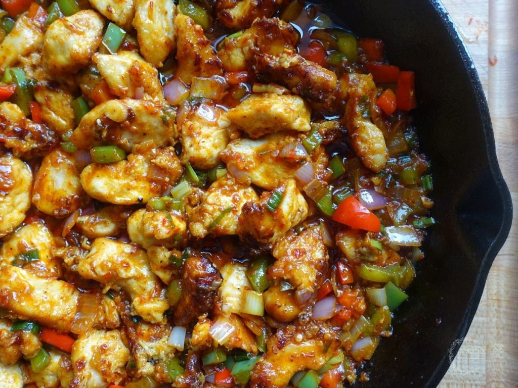 chicken manchurian with manchurian gravy sauce in a cast iron skillet with red bell peppers, green bell peppers, red onion and green onion