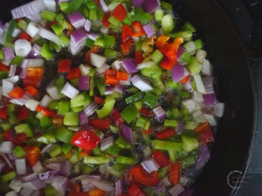 red and green bell peppers, red onion, and green onions sauteing in a cast iron skillet