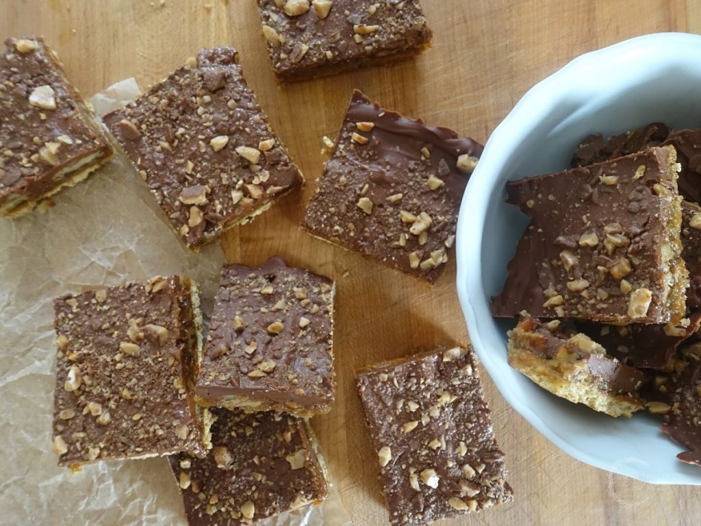 christmas crack using graham crackers on top of parchment paper and some stacked on top of each other in a white bowl 