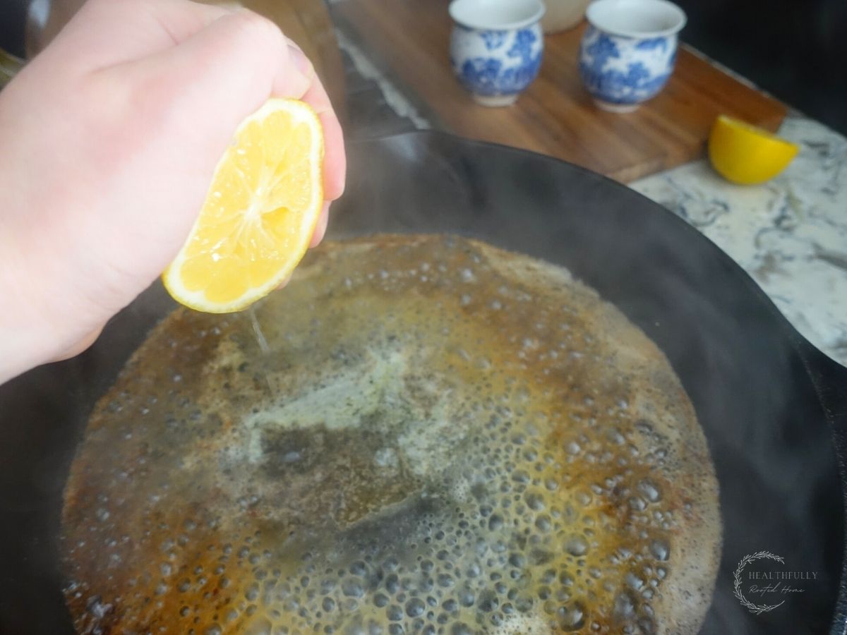 squeezing lemon juice into a cast iron skillet with steam coming off of it and a lemon half in the background