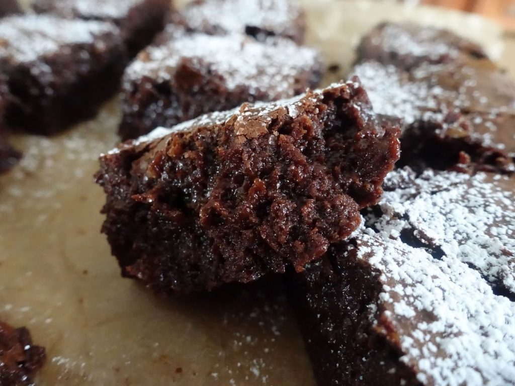 half of a brownie sitting on top another brownie  dusted with powdered sugar