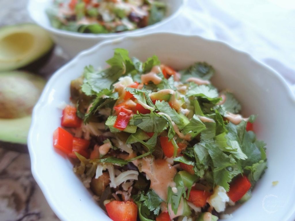 taco bowls with cilantro and sweet potatoes black beans and ground beef in white bowls and halved avocado