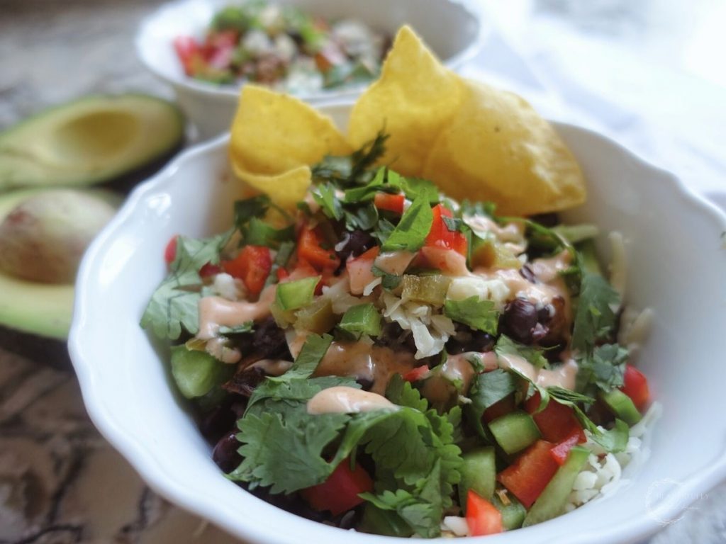 deconstructed taco bowls with avocado on the side and tortilla chips sticking out