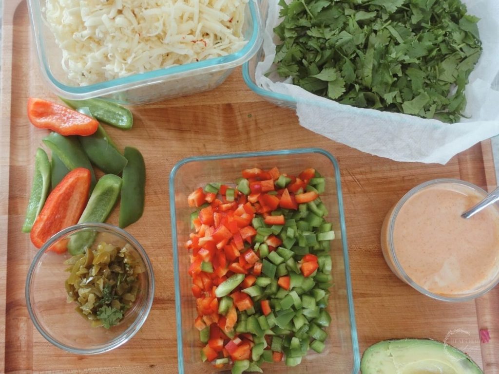 bell peppers jalapenos cilantro shredded pepperjack cheese ancho aioli and avocado all on a wooden boos block cutting board