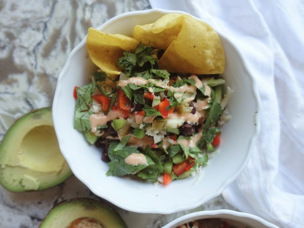 deconstructed taco in a white bowl with tortilla chips ancho aioli cilantro bell peppers and avocado on the side