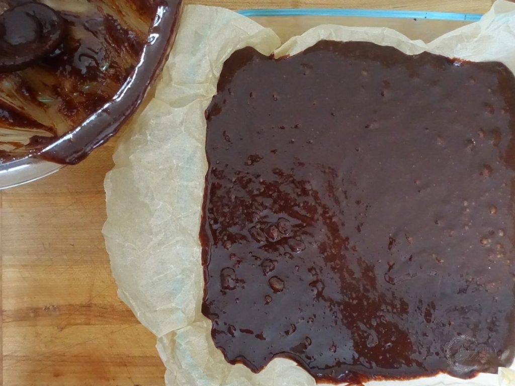 brownie batter in a parchment lined baking dish with the mixing bowl next to it