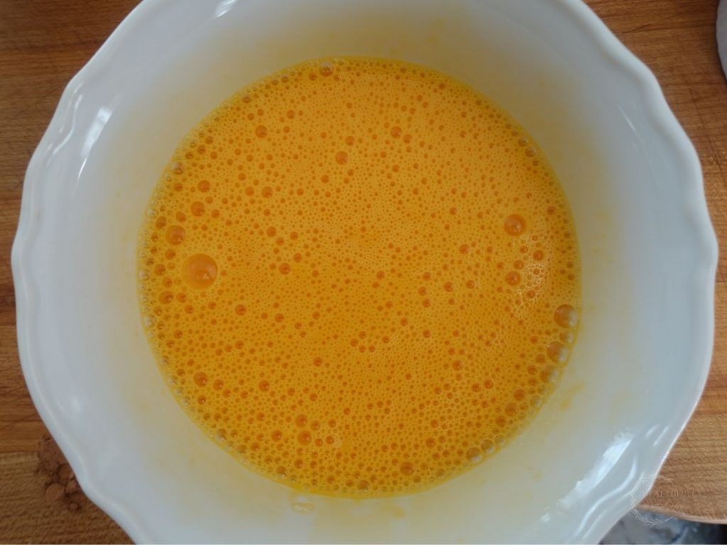 whisked eggs in a white bowl with lots of bubbles on top