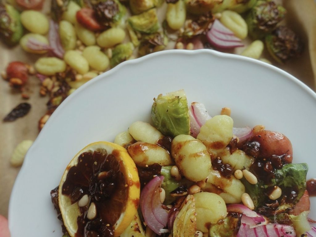 gnocchi tray bake on a white plate with balsamic fig glaze drizzled over top and baking sheet pans in the background