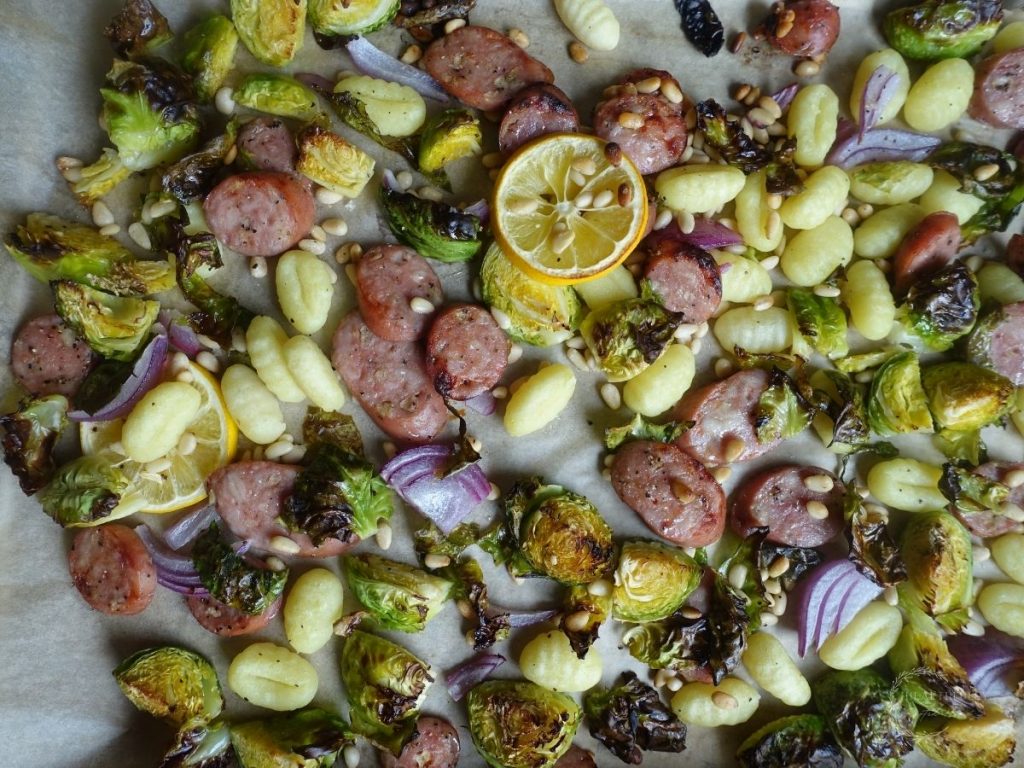 gnocchi tray bake with roasted vegetables and chicken apple sausage and caramelized lemons on a sheet pan with brown parchment paper