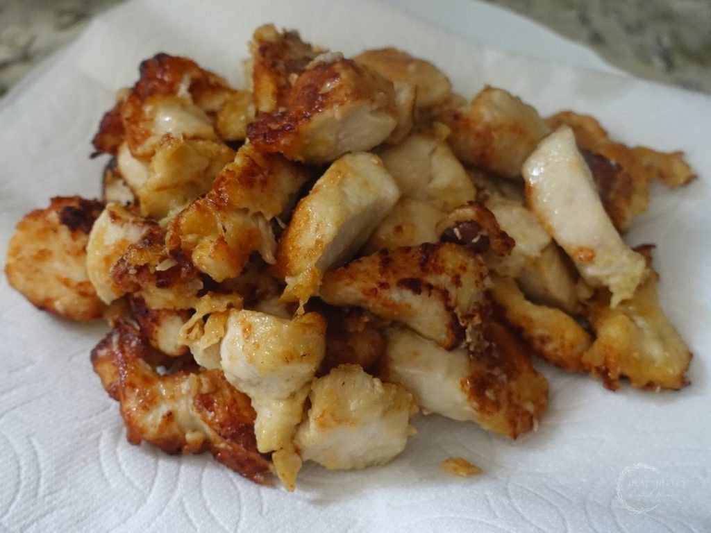 fried chicken on a paper towel lined white plate resting waiting to be added to a chicken manchurian dish with vegetables