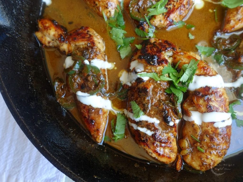 honey jalapeno chicken tenders in a cast iron skillet with honey cream sauce drizzled overtop and garnished with cilantro
