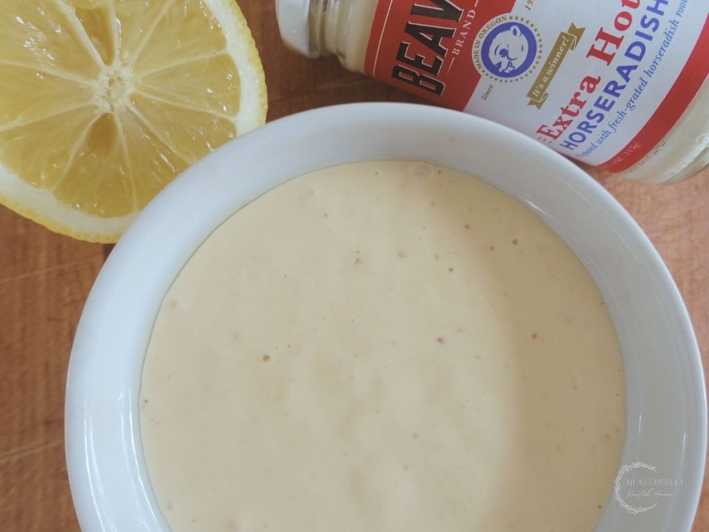 a bowl of horseradish aioli with a lemon wedge in the background along with a jar of prepared horseradish