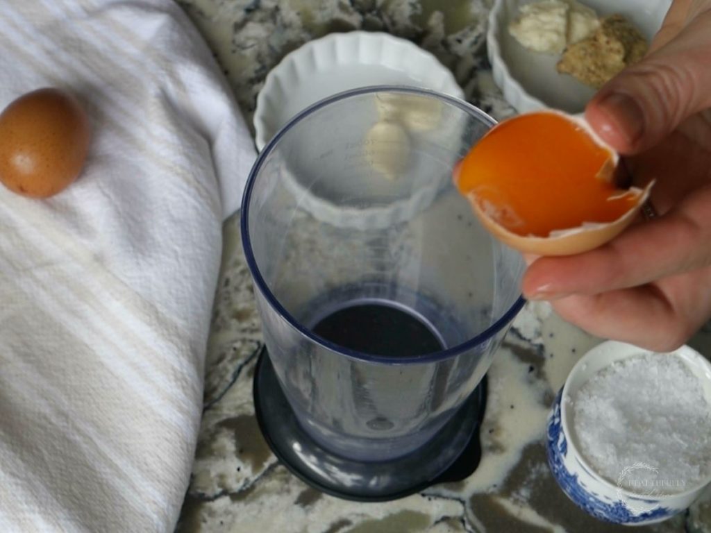 pouring just one egg yolk into the cup of an immersion blender with a bunch of other ingredients surrounding it