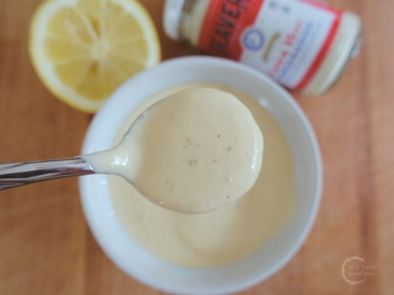 horseradish aioli sauce in a white bowl with a silver spoon scooping some out and a lemon wedge in the background with a jar of beaver horseradish