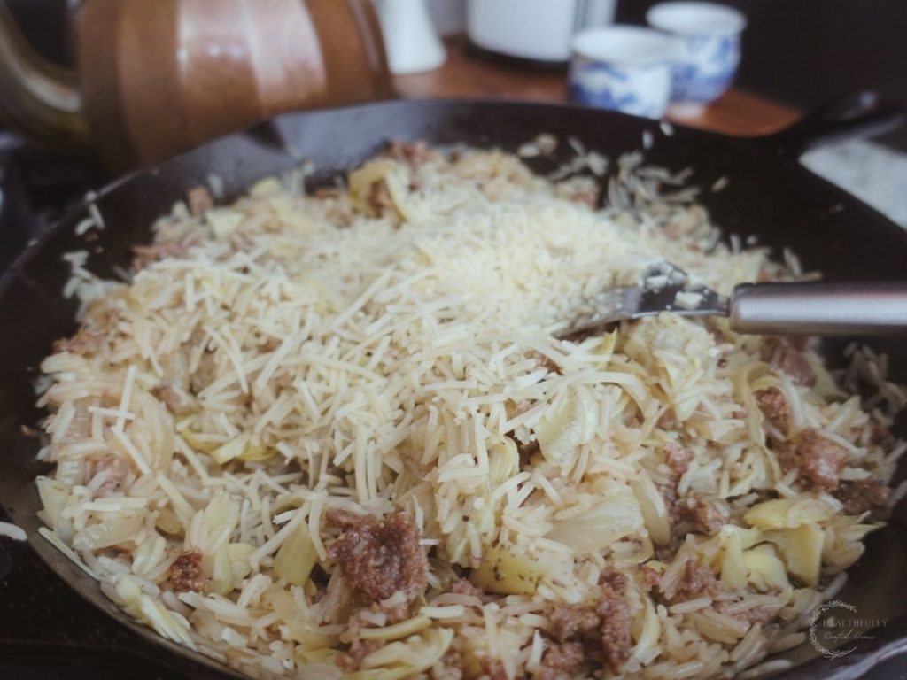 parmesan cheese on top of the risotto basmati in a cast iron skillet with a spatula inside