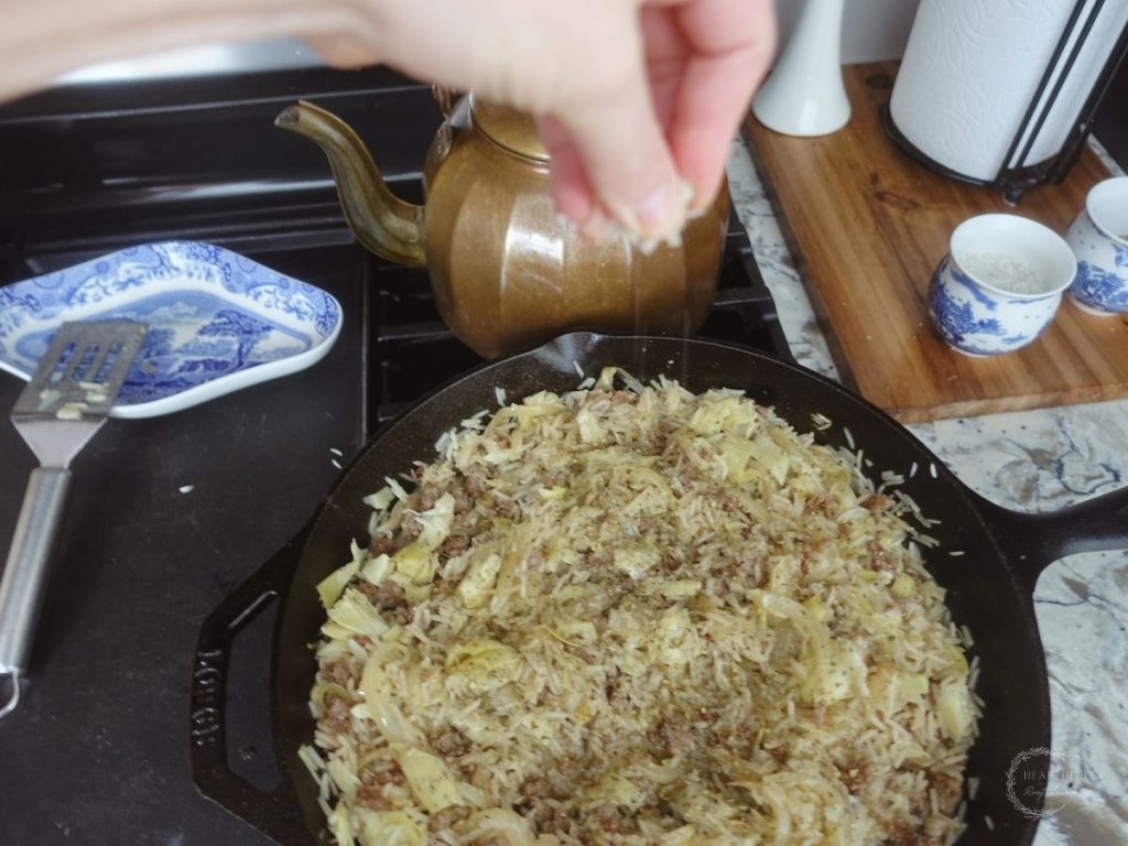 seasoning risotto basmati with sea salt in a cast iron skillet and a spatula and copper tea kettle in the back