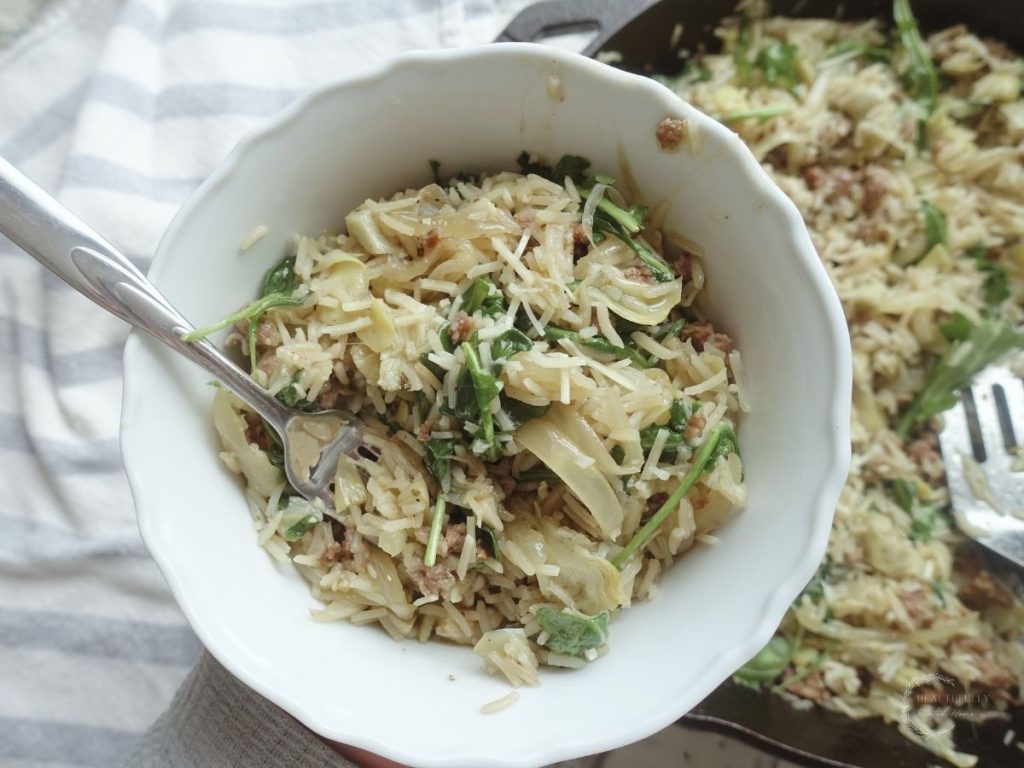 risotto basmati in a white bowl with a silver fork inside above a cast iron skillet with more risotto
