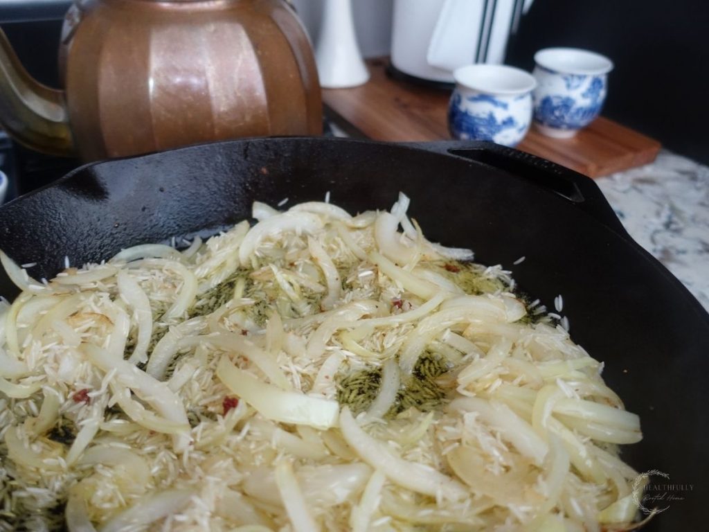 onions and basmati rice in a cast iron skillet with a copper tea kettle in the background