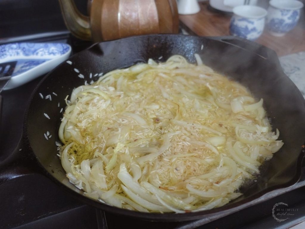 onions and basmati rice with white wine vinegar in a cast iron skillet with a copper tea kettle behind it