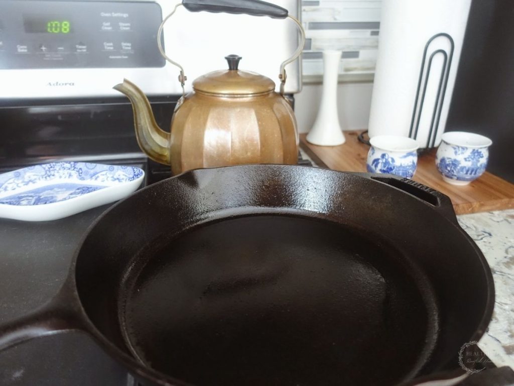 cast iron skillet preheating on a gas stovetop with a copper tea kettle and blue and white china in the background