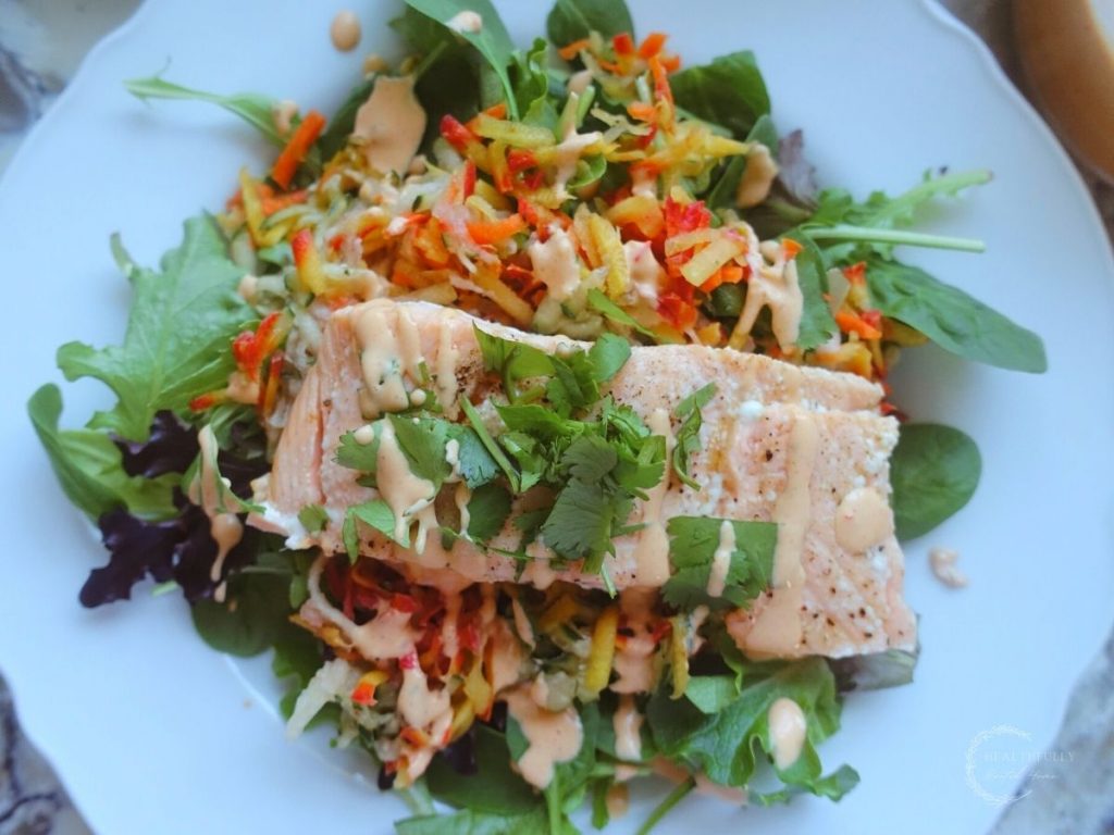 salmon banh mi salad on a white plate topped with cilantro on a bed of spring greens