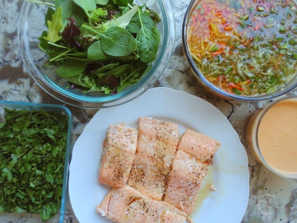 cooked salmon on a white plate pickled vegetables in a glass container spring greens in a glass bowl and ancho aioli in a glass bowl