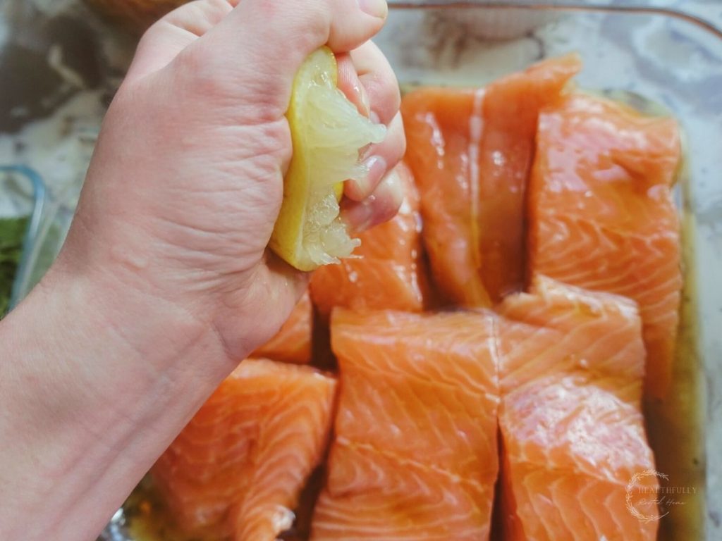 squeezing lemon juice overtop salmon in a baking dish 