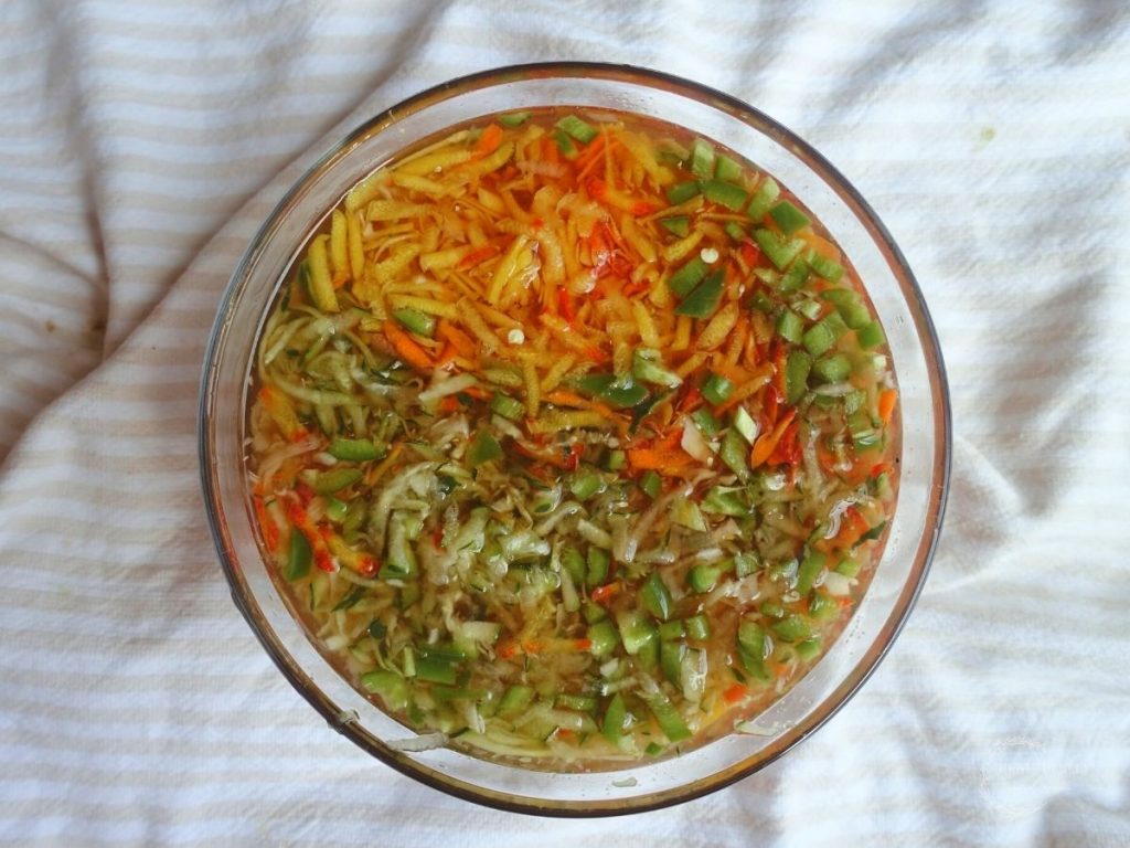 quick pickled vegetables in a glass bowl overtop a white and cream colored ticking stripe tea towel