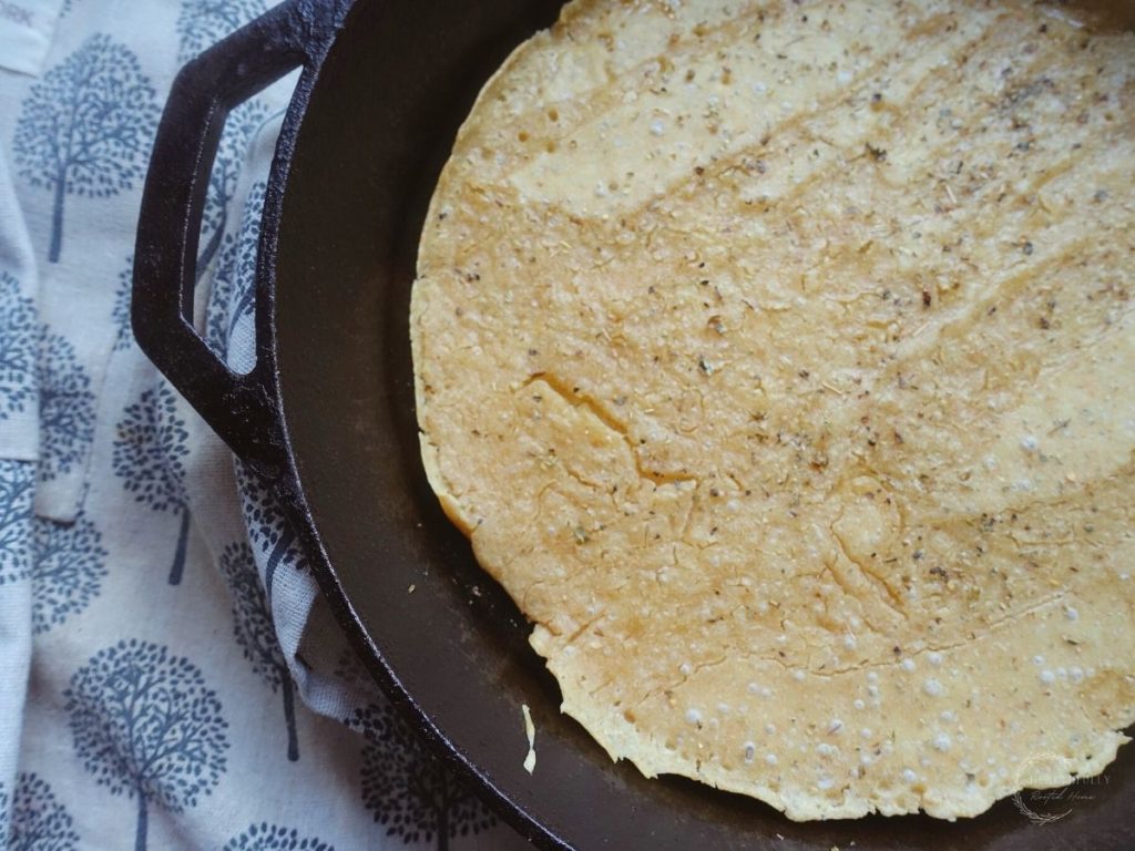 same day sourdough pizza crust in a cast iron skillet with an apron next to it