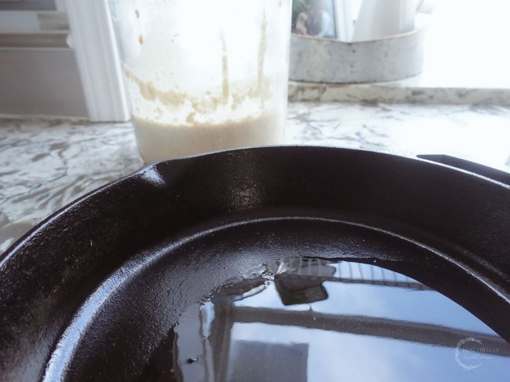 avocado oil on a preheated cast iron skillet with sourdough starter in the background
