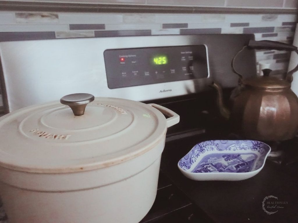 oven range with a white cast iron dutch oven and a copper tea kettle and oven preheating to 425