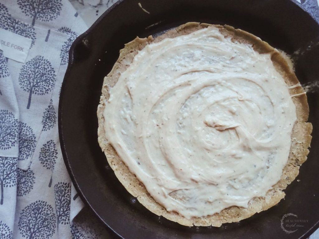 white sauce spread over a sourdough pizza crust in a cast iron skillet