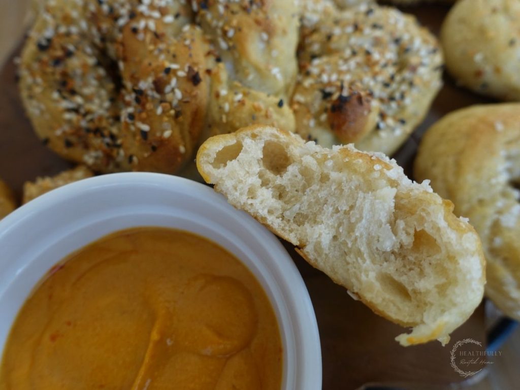 healthy soft long fermented sourdough pretzels on a wooden block with one ripped in half so you can see the soft inside leaning up against some cheese sauce