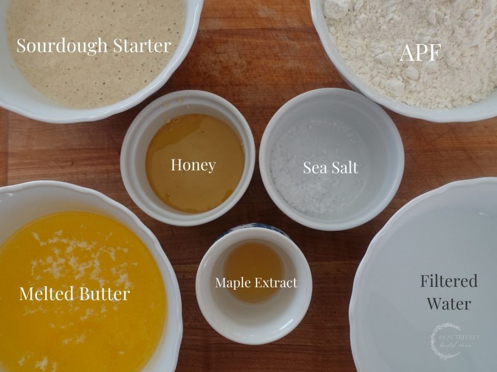 ingredients for sourdough monkey bread dough in white bowls on a wooden cutting board with labels saying what they are