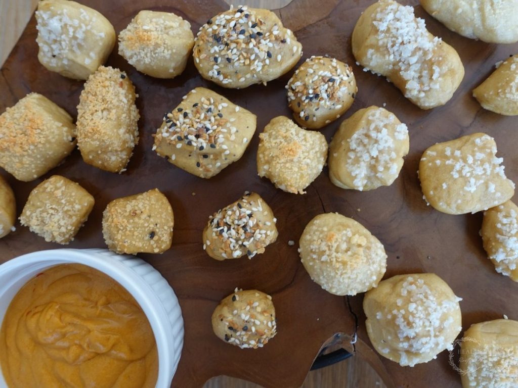 sourdough pretzel bites with various toppings on a wooden block next to a white bowl of cheese sauce