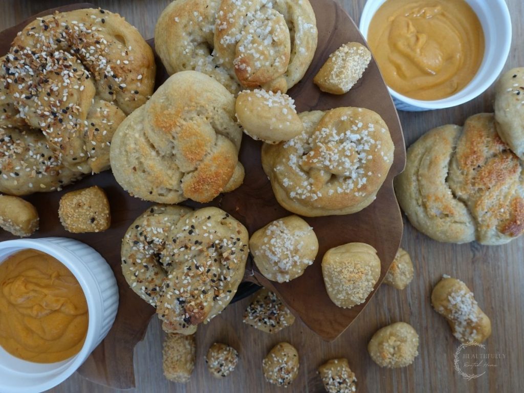 sourdough pretzels on a wooden block next to some cheese sauce and sourdough pretzel bites