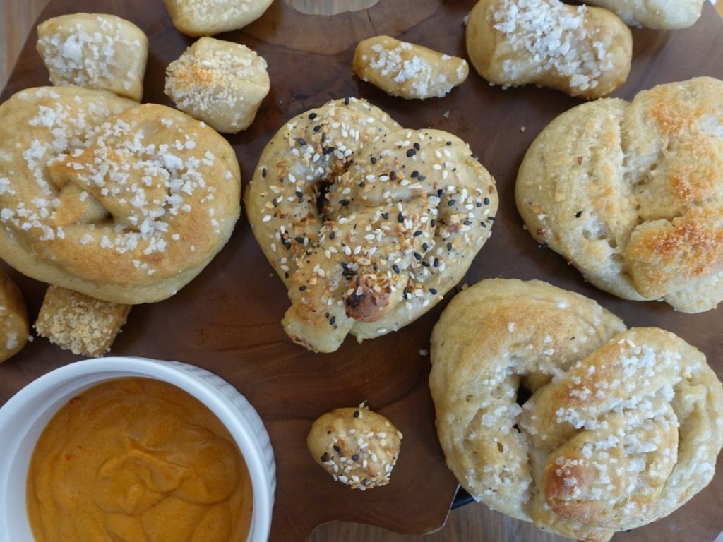 sourdough pretzels with various toppings next to some cheese sauce
