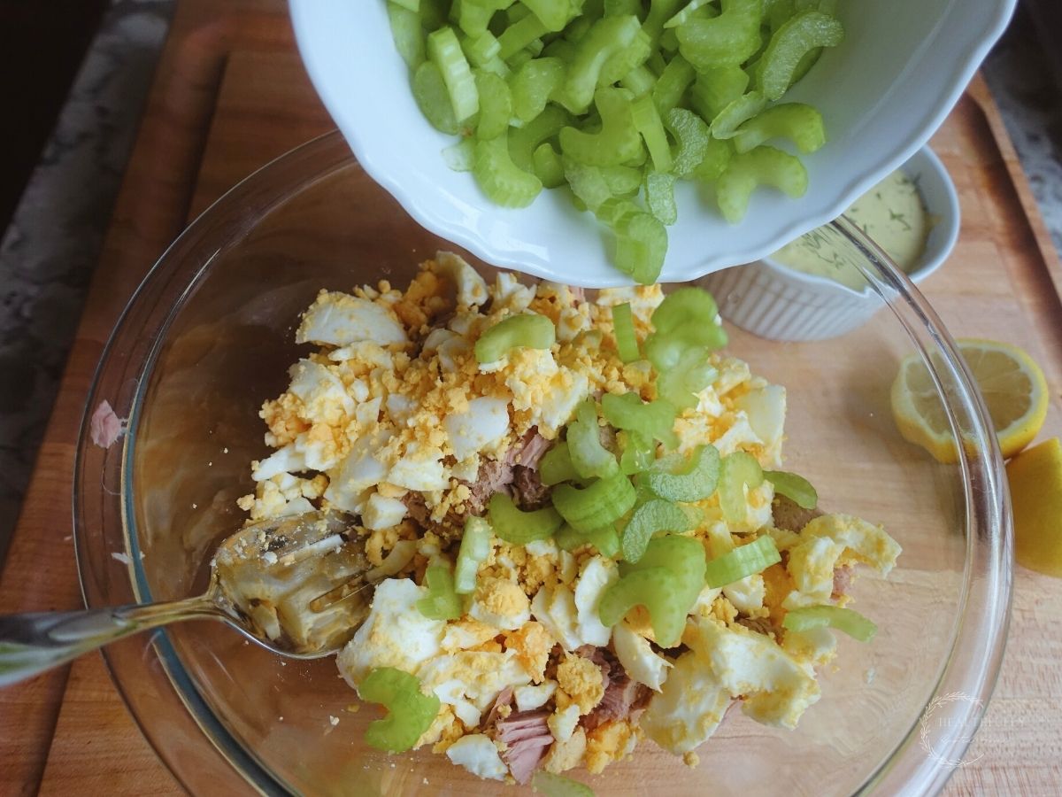 pouring chopped celery into a bowl with eggs and tuna salad