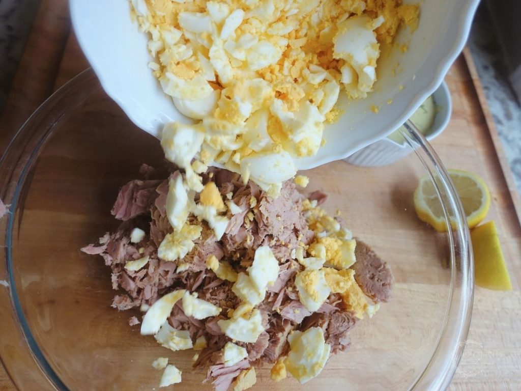 pouring hard boiled eggs into a glass bowl with tuna fish