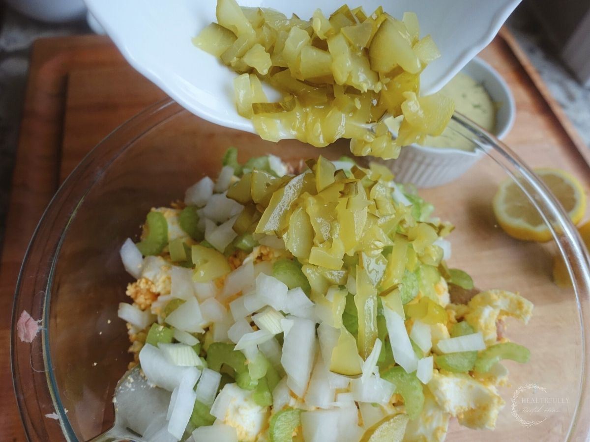 pouring pickles into a bowl with tuna salad