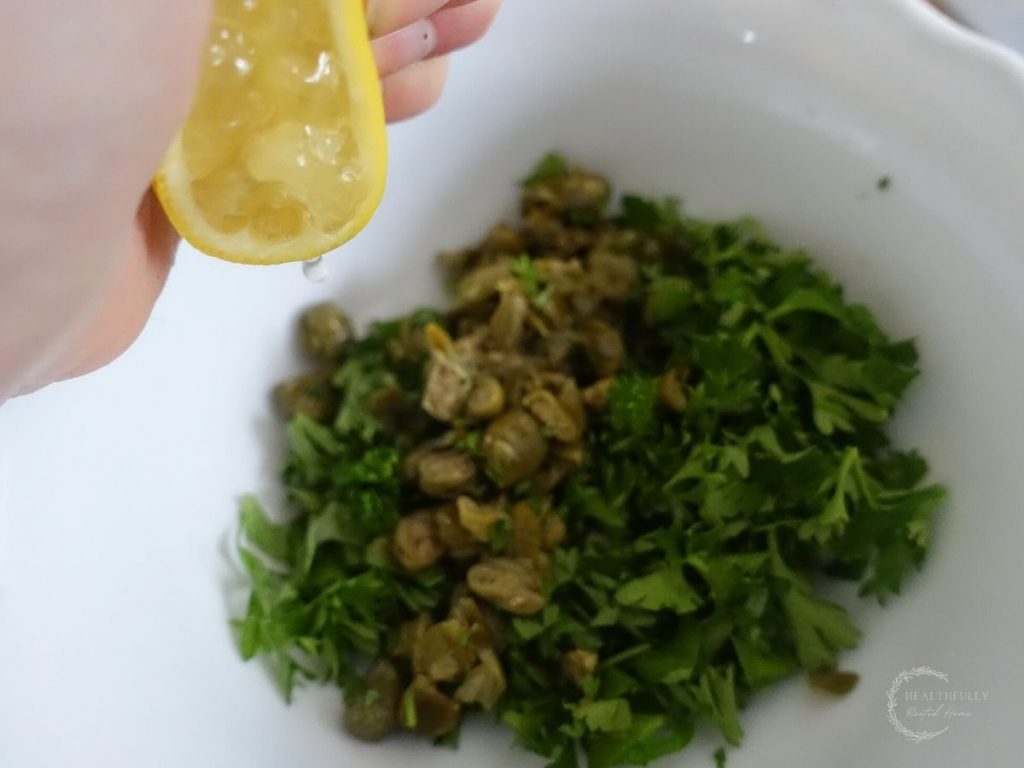 squeezing lemon juice overtop salsa gremolata in a white bowl