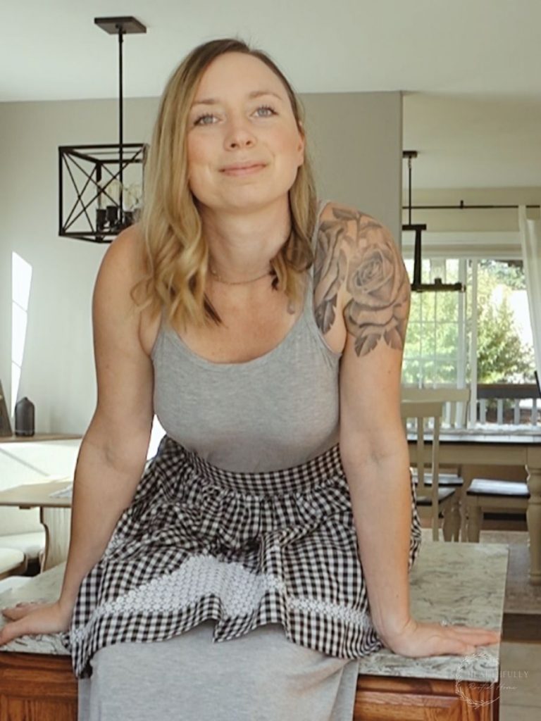 kyrie of healthfully rooted home wearing a long grey dress with a vintage black and white checkered waist apron 