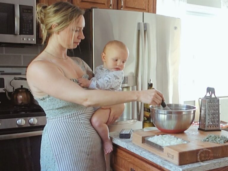 woman holding a baby while wearing a half apron and making dinner