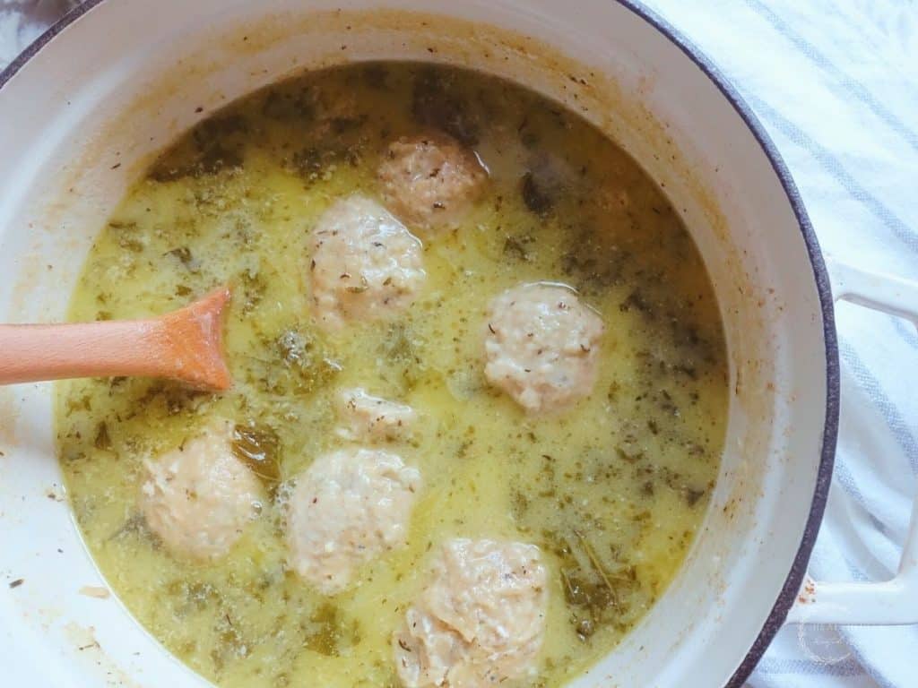 sourdough dumplings in a white dutch oven with chicken kale soup and homemade bone broth