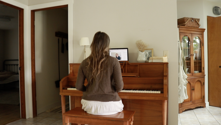 A Christian homemaker in a brown sweater and gingham dress sits at her piano.