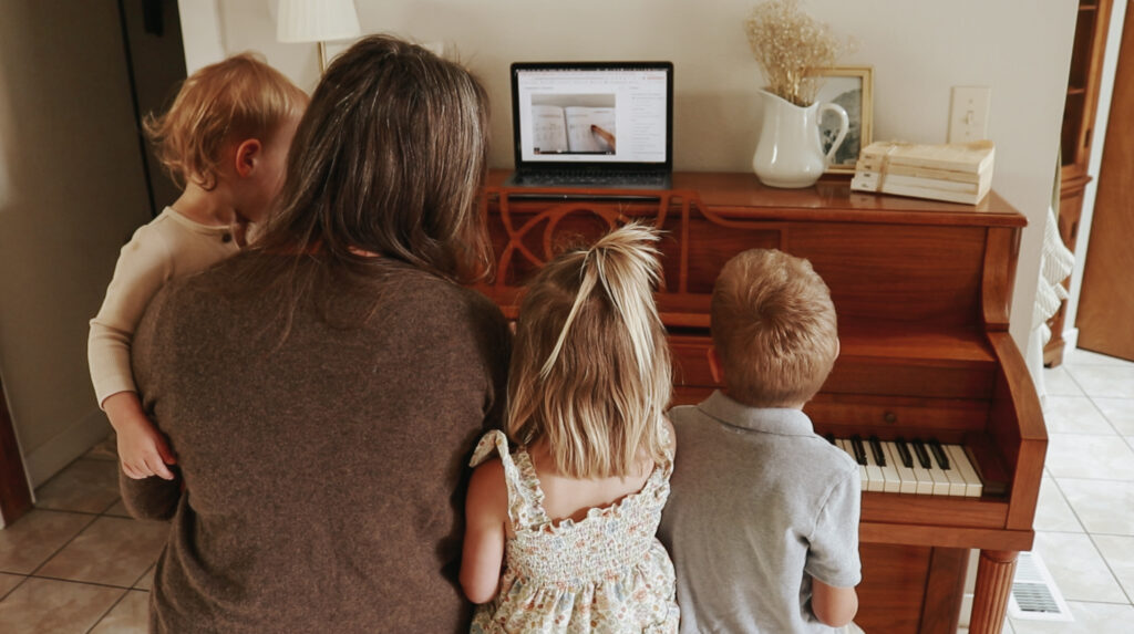 A Christian homemaker and her three children sit at a piano and watch a music lesson.